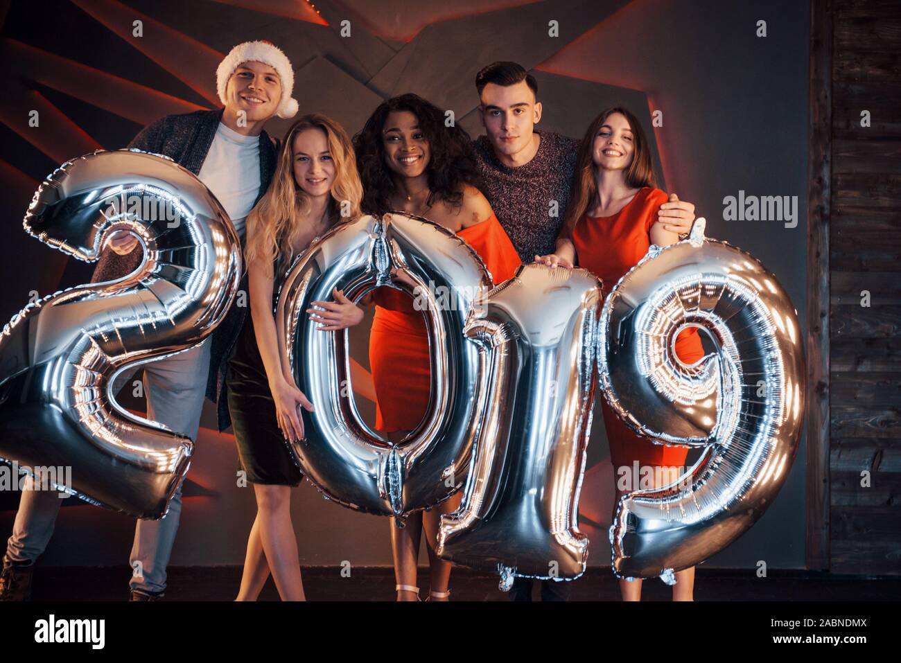 Il nuovo 2019 si avvicina. Un gruppo di giovani allegri gente multinazionale in Santa's hat con numeri di argento e gettando i confetti al partito. Felice Foto Stock