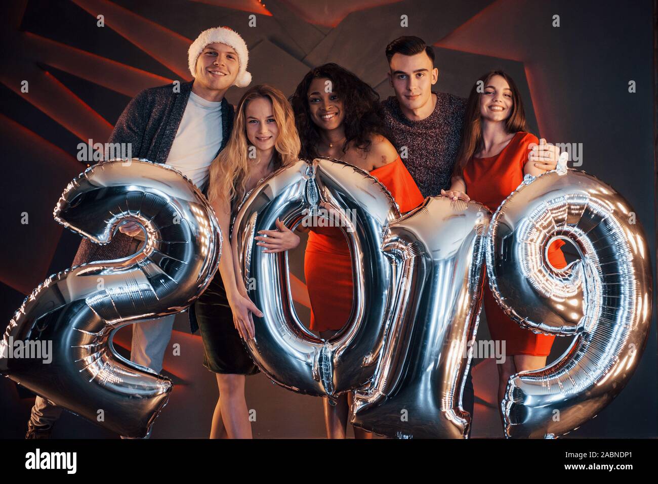 Il nuovo 2019 si avvicina. Un gruppo di giovani allegri gente multinazionale in Santa's hat con numeri di argento e gettando i confetti al partito. Felice Foto Stock