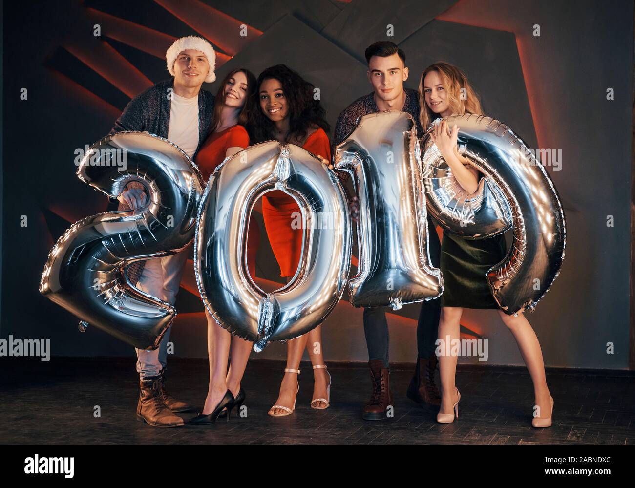 Il nuovo 2019 si avvicina. Un gruppo di giovani allegri gente multinazionale in Santa's hat con numeri di argento e gettando i confetti al partito. Felice Foto Stock