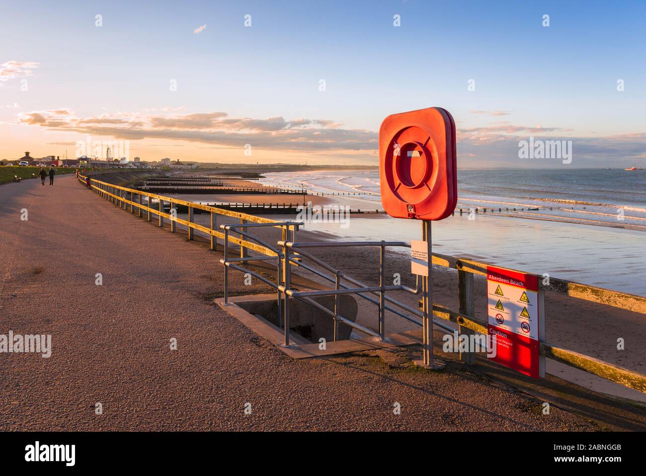 Salvagente su un sentiero recintato sul Seawall lungo una bellissima spiaggia al tramonto Foto Stock
