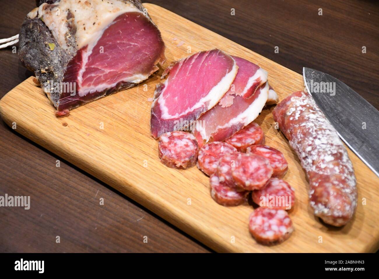 Fette di materie salati prosciutto casalingo o prosciutto e salsiccia su una tavola di legno con il coltello Foto Stock