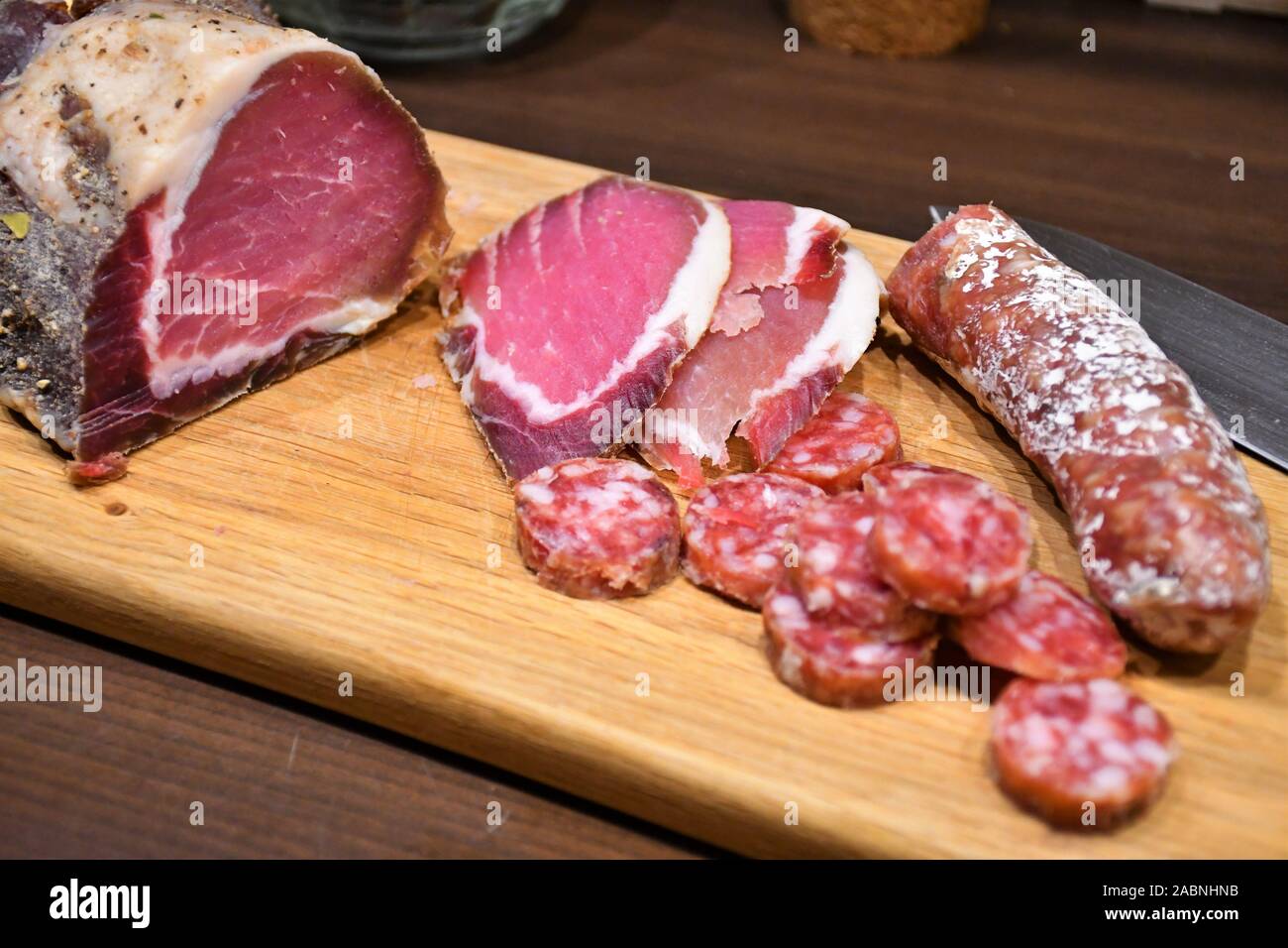 Fette di materie salati prosciutto casalingo o prosciutto e salsiccia su una tavola di legno con il coltello Foto Stock