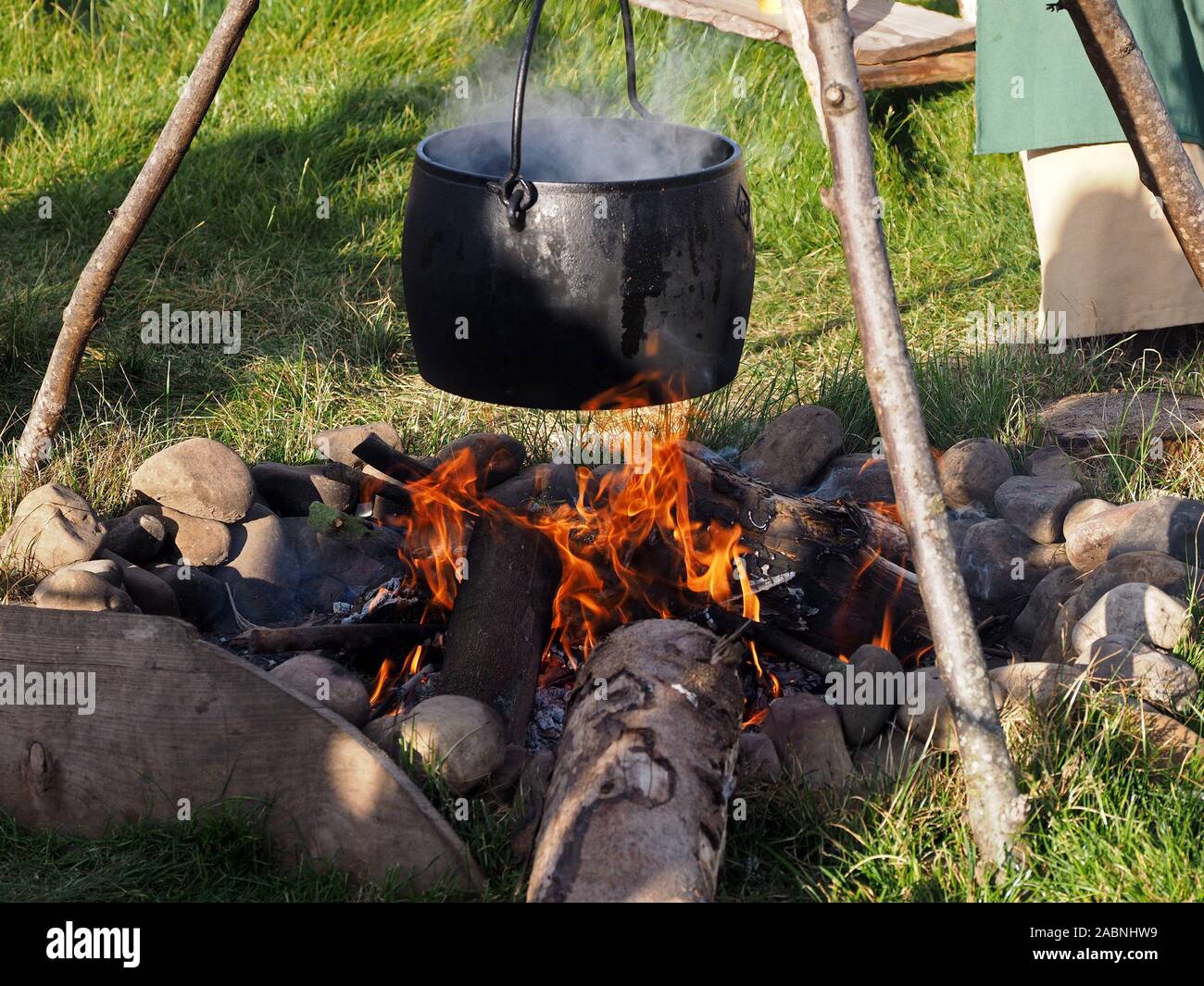 Curling in fiamme sotto il fumo nero pentola di cottura appeso stick treppiede su fuoco di campo alla ricostruzione di Viking camp nella Contea di Durham, England, Regno Unito Foto Stock