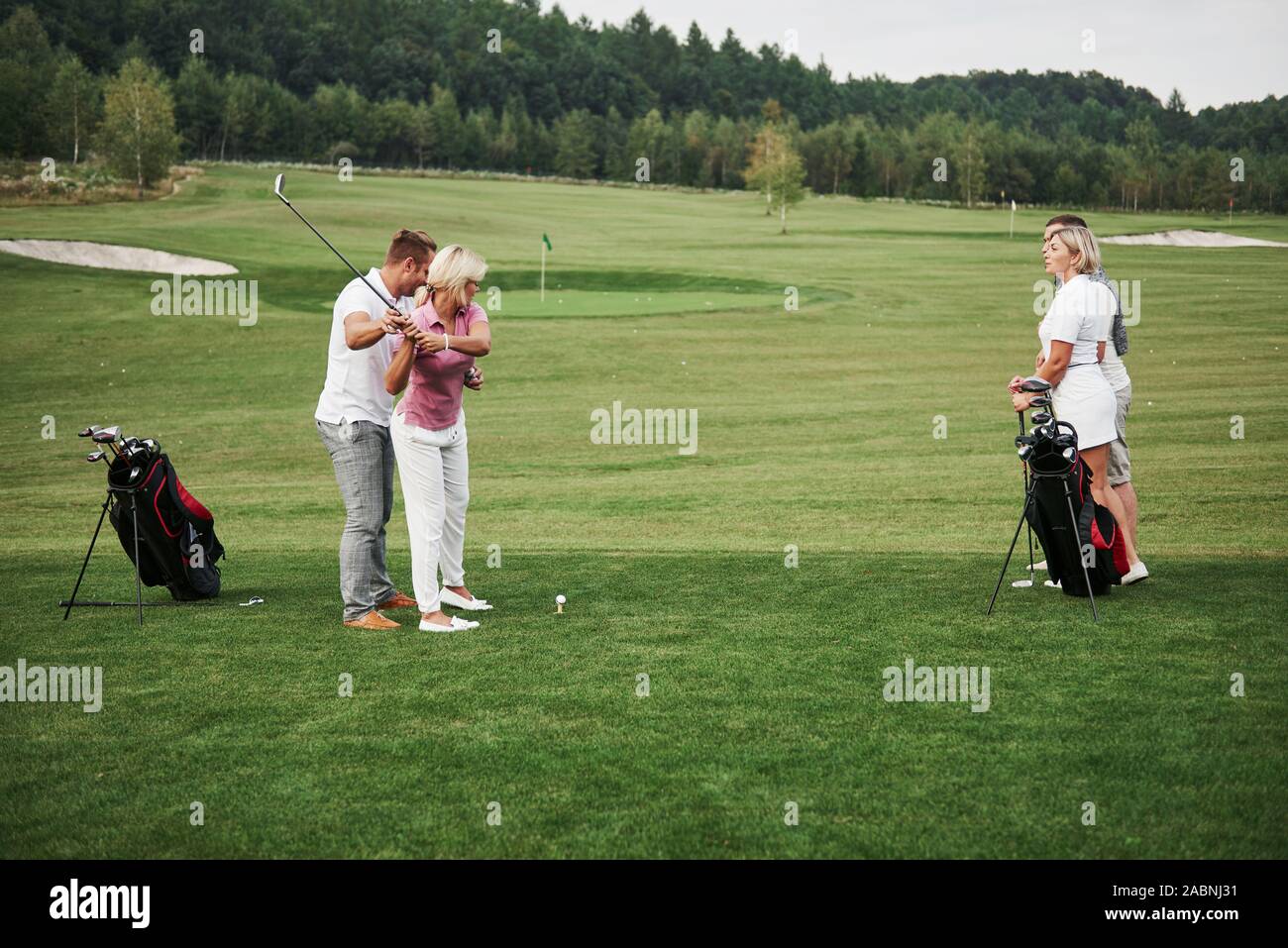 Ragazza che gioca a golf e colpendo da putt sul verde. Il suo insegnante aiuta a esplorare la tecnica ed eseguire il suo primo scioperi Foto Stock