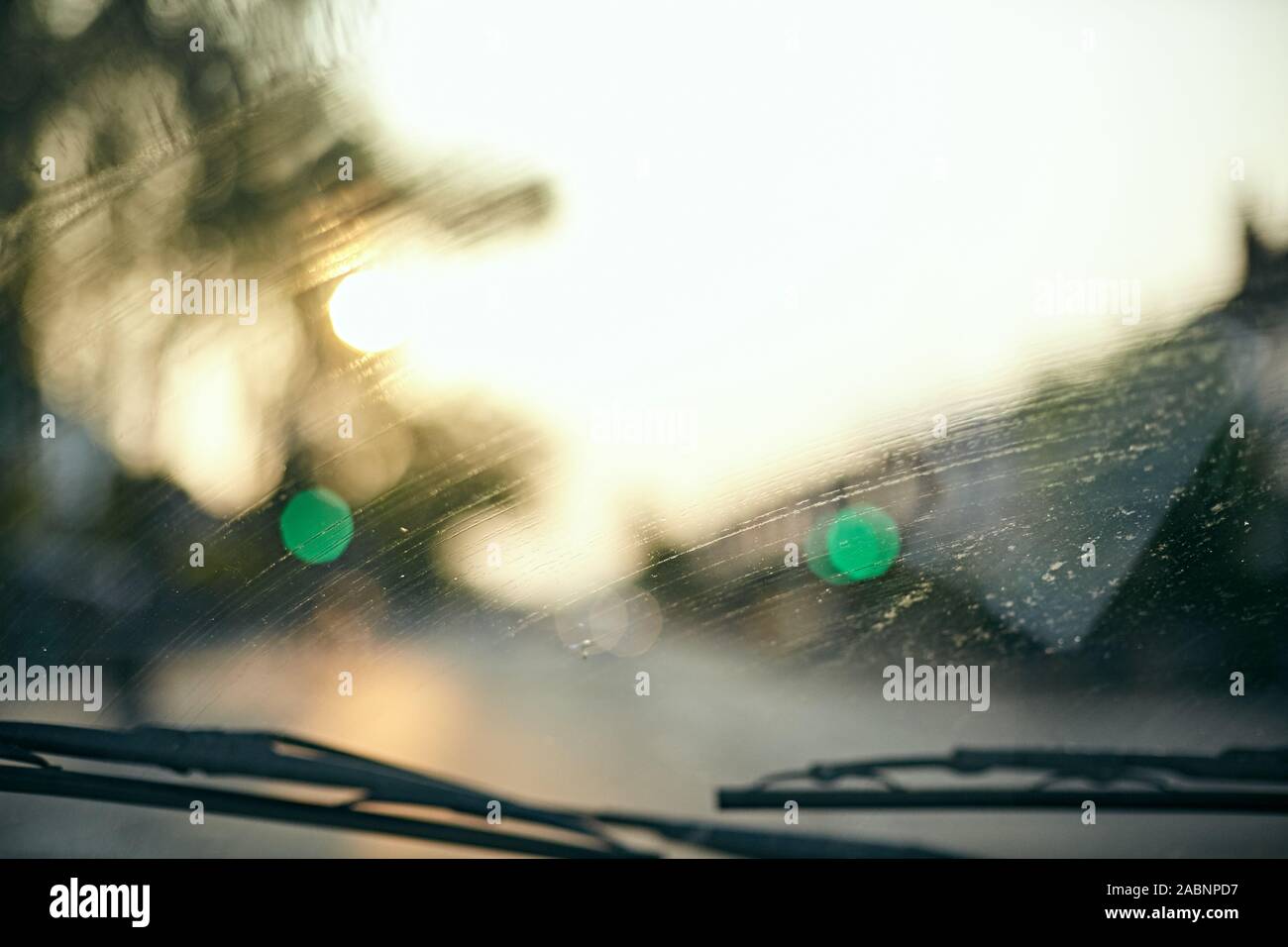 Sfocata vista fuori da un auto parabrezza anteriore con un tramonto, traffico verde luci e tergivetri del parabrezza Foto Stock