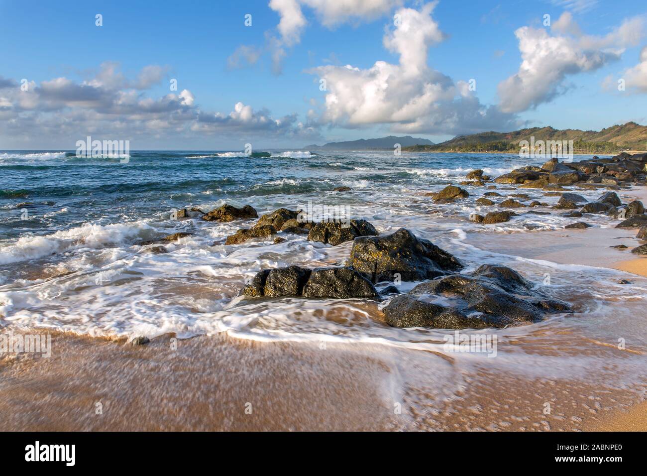 High surf e onde intorno le rocce vulcaniche su di una spiaggia di sabbia appena dopo il tramonto su una mattina nuvoloso con gara della luce del sole, Kapa'a Kauai, Hawaii Foto Stock