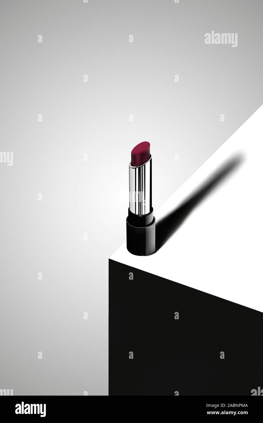 Un rossetto rosso sul bordo di un quadrato il podio con una forte ombra su uno sfondo bianco Foto Stock
