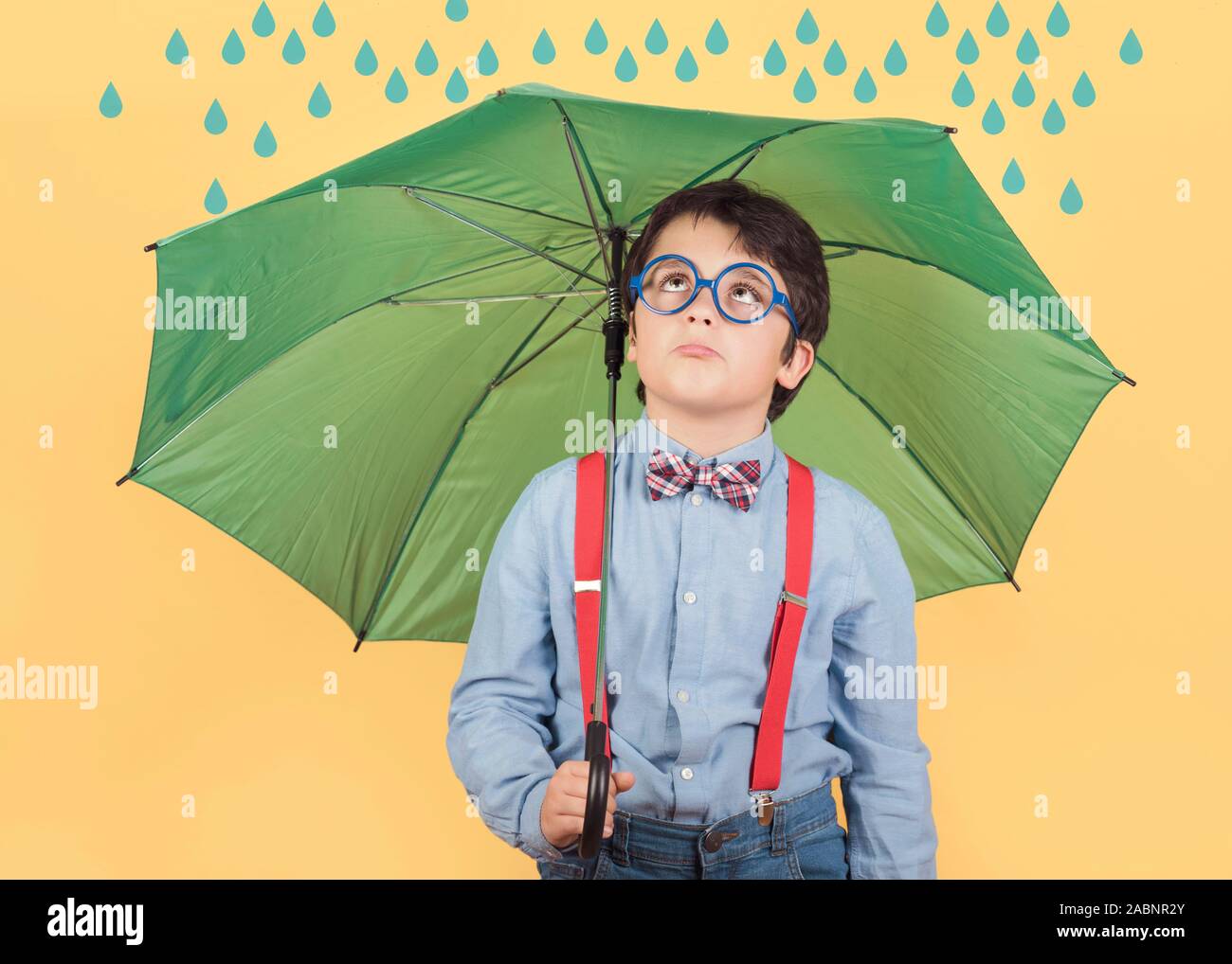 Bambino con ombrello verde su sfondo giallo Foto Stock