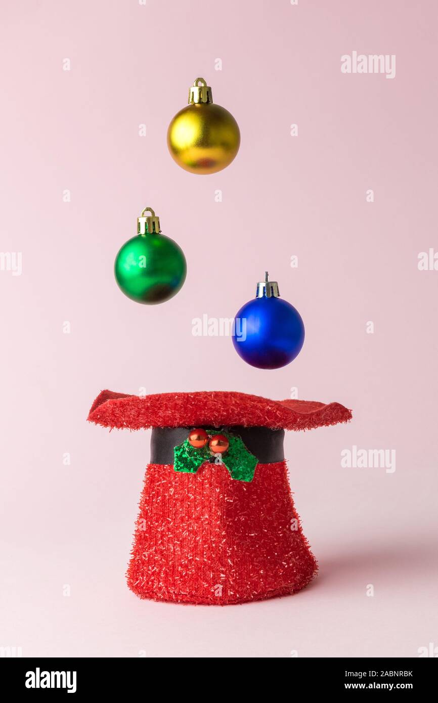 Colorate decorazioni di Natale baubles di cadere nella hat contro di rosa pastello minimo background creativo il concetto di vacanza. Foto Stock