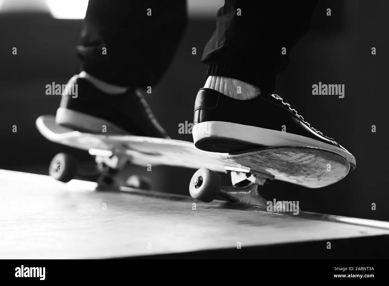 Un'immagine in bianco e nero di un uomo di piedi, vestiti in modo elegante sneakers, facendo scorrere su uno skateboard su una rampa. Foto Stock
