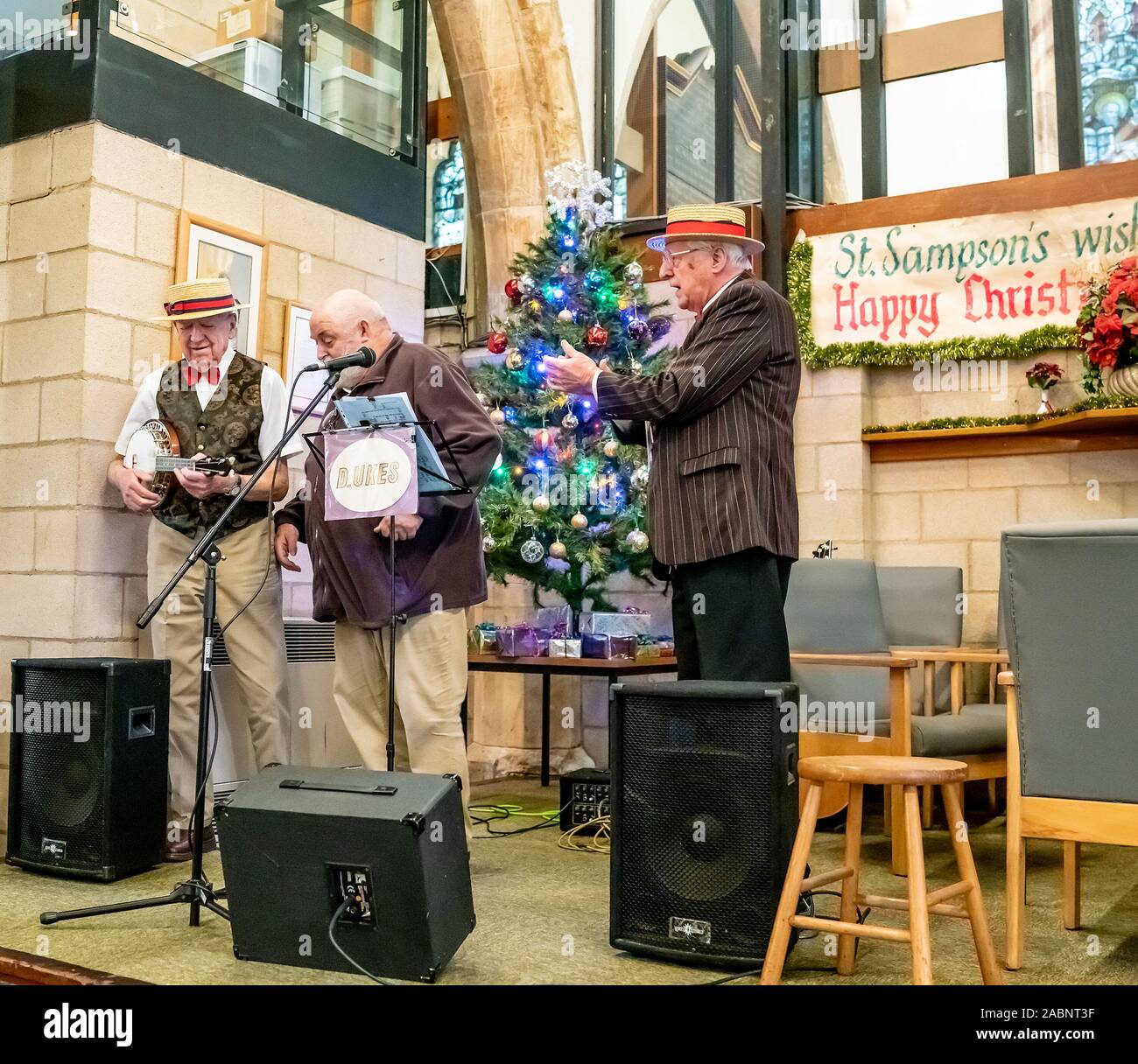Due anziani signori giocando l'ukulele accompagnato da un vocalist maschio ad una festa di Natale il caffè la mattina in St Sampson la Chiesa in York Foto Stock Due anziani signori giocando l'ukulele accompagnato da un vocalist maschio ad una festa di Natale il caffè la mattina in St Sampson la Chiesa in York Foto Stock