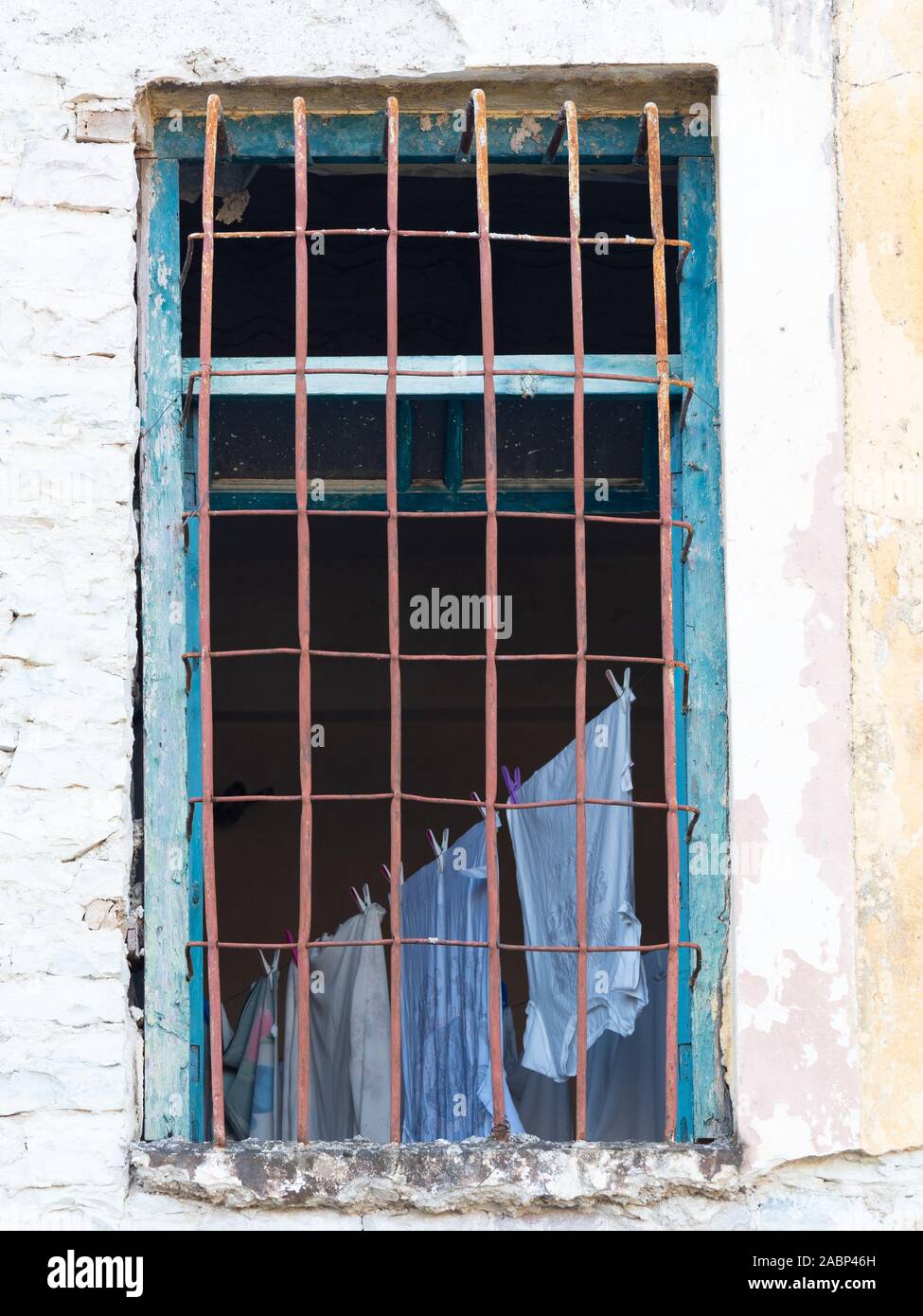 Argirocastro, Albania - biancheria lavata appeso su uno stendibiancheria fotografato attraverso una finestra con barre di metallo e scheggiati turchese del rivestimento del vetro. Foto Stock