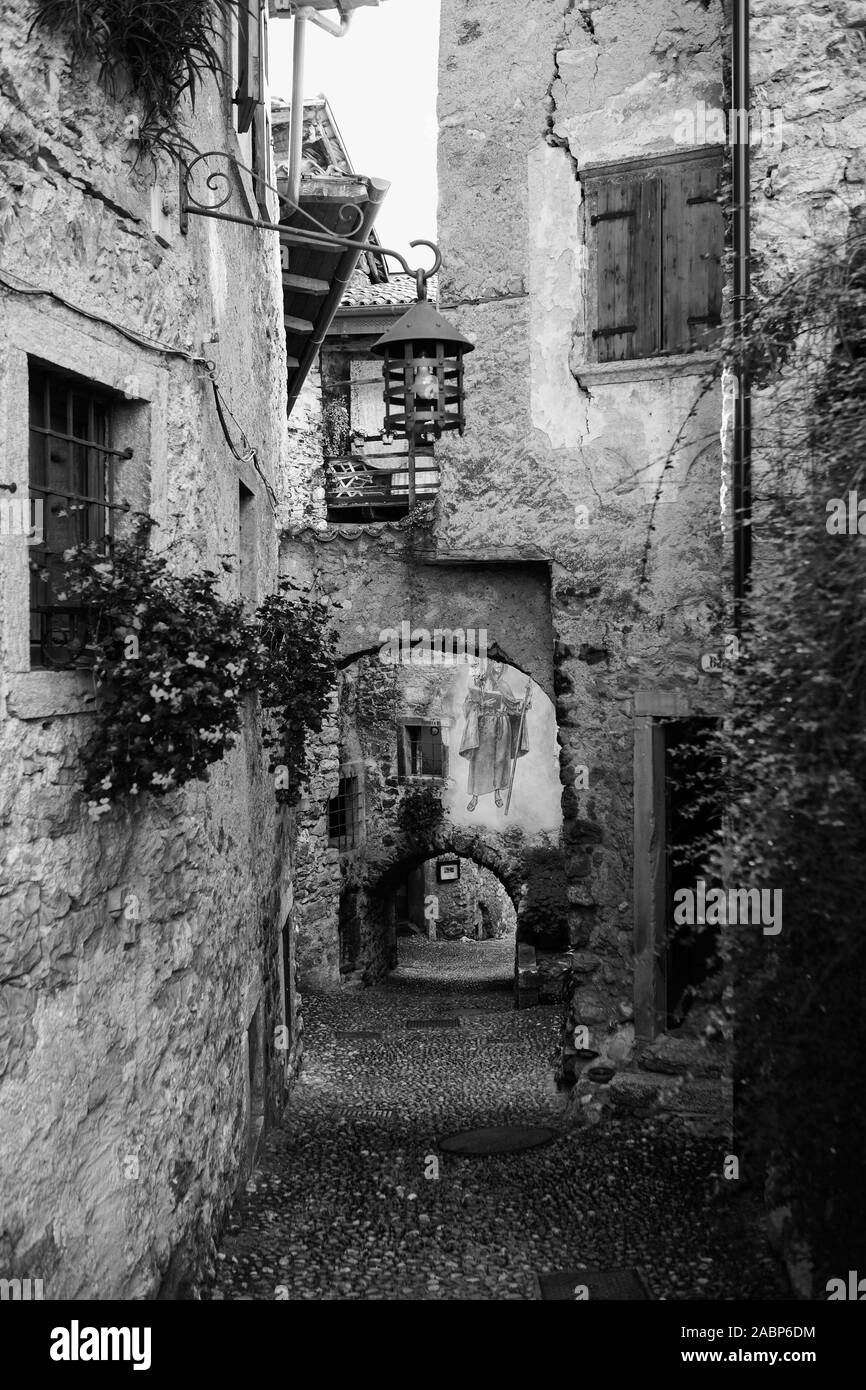Via Fratelli Bandiera, una stretta viuzza attraverso archi a tunnel, Canale di Tenno, Trentino-Alto Adige, Italia. Versione in bianco e nero Foto Stock