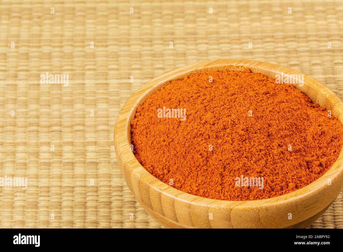 Ciotola piena di peperoncino in polvere su un sfondo di bambù Foto Stock