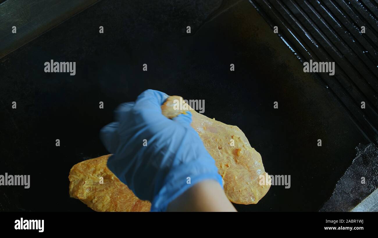 Vista dall'alto lo Chef mette la carne cruda sul grill. Marinata di filetto di pollo fritto Foto Stock