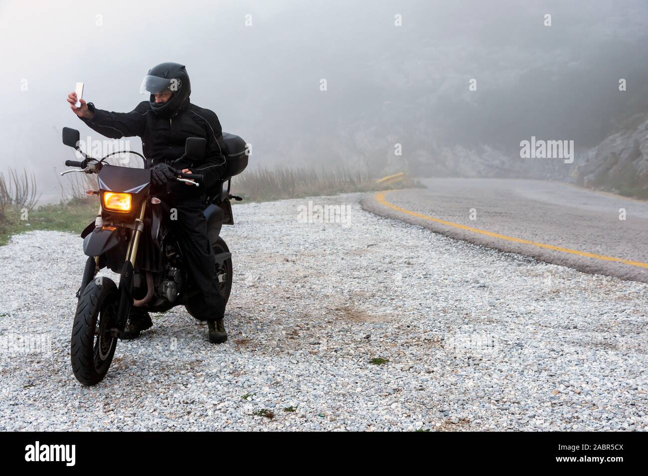 Rider è il tentativo di trovare il segnale sul suo cellulare su un nebbioso giorno ride su per le montagne con la sua moto - avventura progetto ride Foto Stock