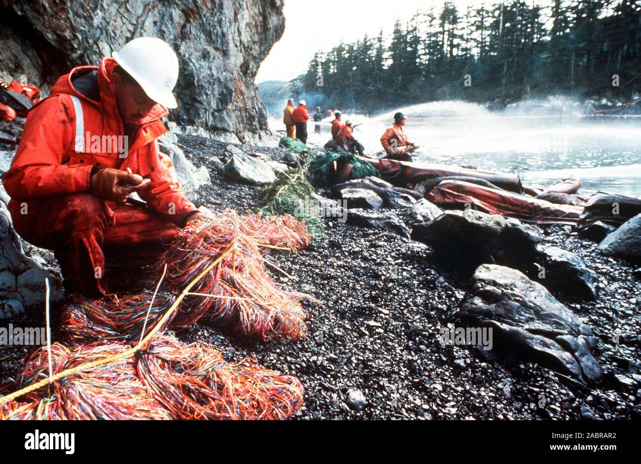 Prince William Sound, AK (Mar. 28)--Coast Guardsman controlli di recupero olio mesh come altri sbuffo di vapore rocce e coste bagnare con olio grezzo dalla fuoriuscita di petroliera Exxon Valdez. La Exxon Valdez si è arenata sulla Bligh Reef in Prince William Sound, Alaska, 23 marzo 1989 la fuoriuscita di 11 milioni di galloni di petrolio greggio che ha provocato la più grande marea nera nella storia degli Stati Uniti. Foto Stock