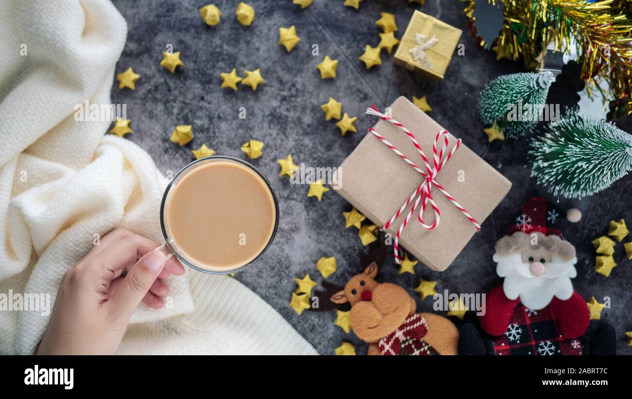 Mano che regge una tazza di caffè caldo nella stagione invernale con sfondo di Natale decorazioni e confezioni regalo su tavola Foto Stock