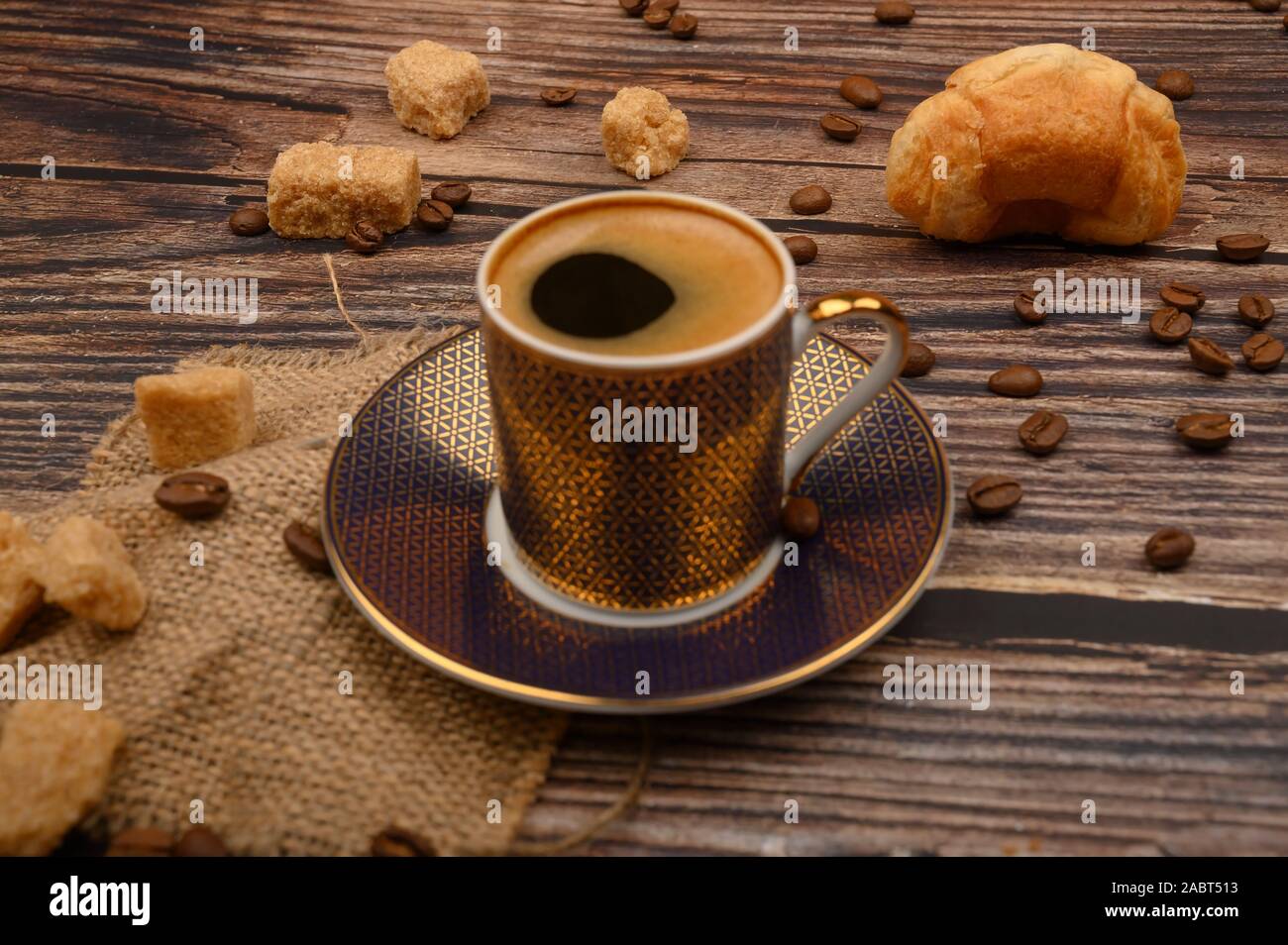Tazza da caffè, croissant, lo zucchero di canna e i chicchi di caffè su sfondo di legno. Close up Foto Stock