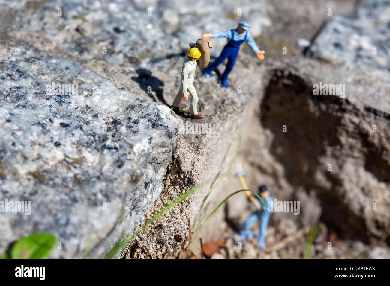 Lavoratore in miniatura con un martello che lavora in una cava, mentre un istruttore che dà ordini e altri lavoratori sono vicini Foto Stock