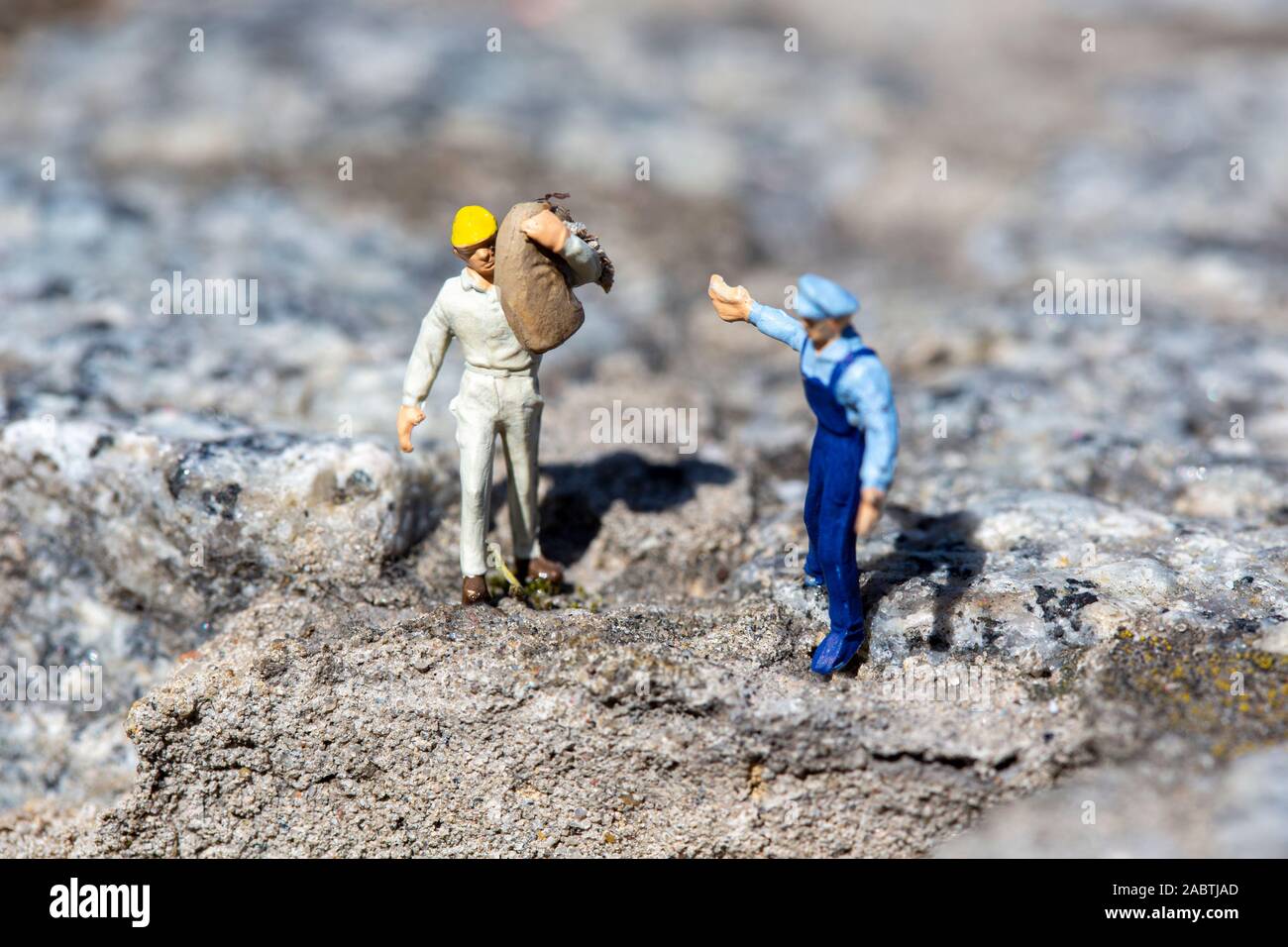Lavoratore in miniatura con un martello che lavora in una cava, mentre un istruttore che dà ordini e altri lavoratori sono vicini Foto Stock