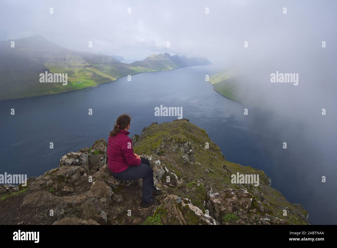 Solo femmina viaggiatore seduto su una roccia, guardando fuori sulle isole nordest e fiordi, le Isole Faroe Foto Stock