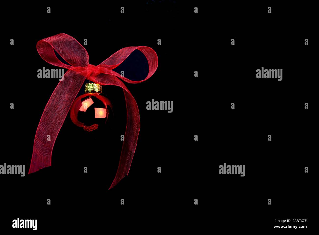 Nero copia di Natale spazio con sfera rossa appeso con un rosso organza bow su sfondo nero Foto Stock