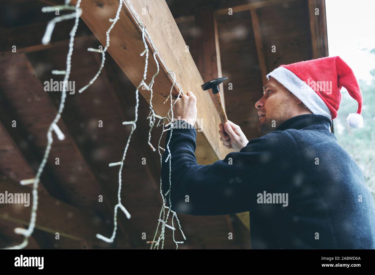 L'uomo con il cappello da Babbo Natale Decorare casa carport per esterni con natale luci di stringa Foto Stock