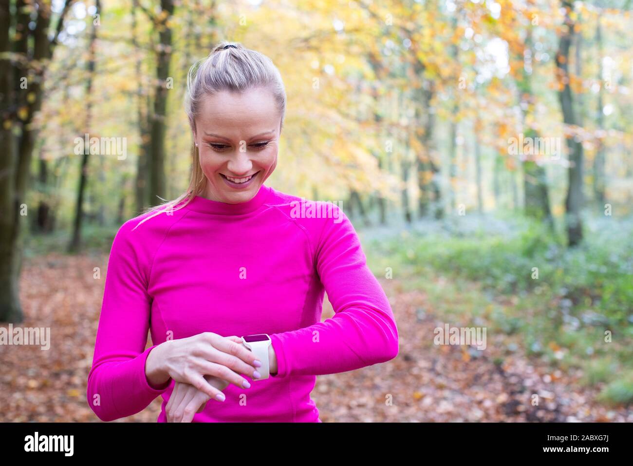 Donna che esercitano nel bosco in Autunno Guardando il tracker di attività su Smart Watch Foto Stock