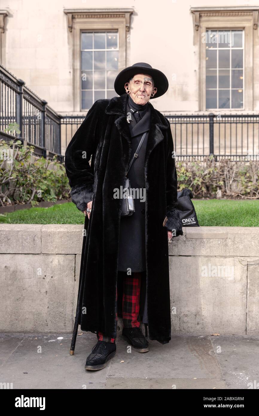 A piena lunghezza Ritratto di un uomo di mezza età con piercing e tatuaggio sul suo viso e le orecchie e indossando un cappello lungo nero pelliccia, Londra, Inghilterra, Regno Unito. Foto Stock