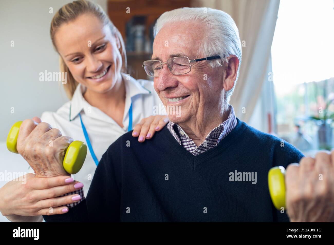 Fisioterapista femmina Senior aiuta l uomo a sollevare pesi a mano a casa Foto Stock