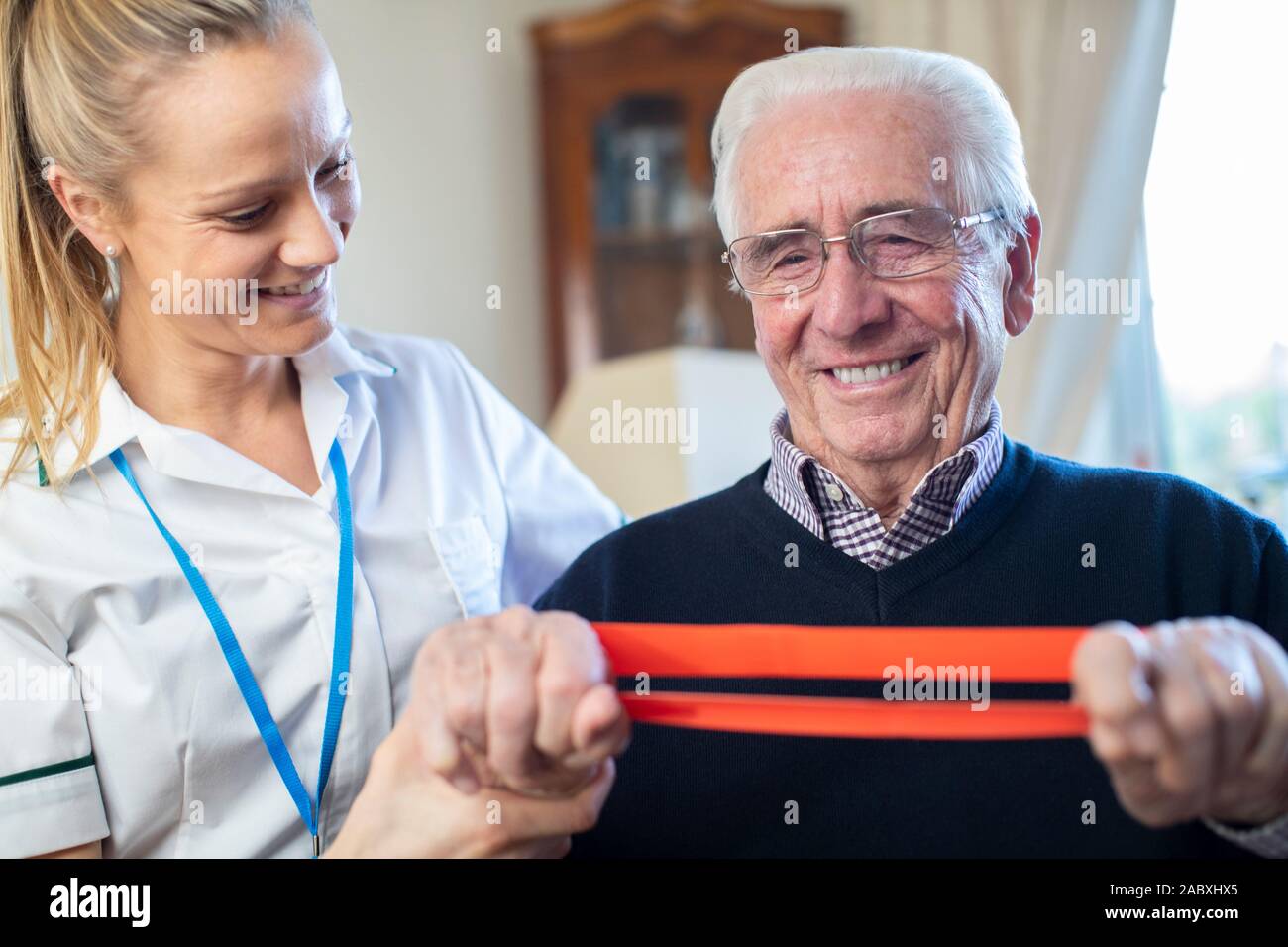 Fisioterapista femmina Senior aiuta l uomo a utilizzare la banda di resistenza a casa Foto Stock