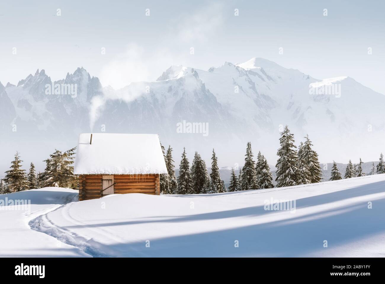 Fantastico paesaggio invernale con casa in legno in montagna innevata. Il fumo proviene dal camino della coperta di neve capanna. Vacanze di Natale concept Foto Stock