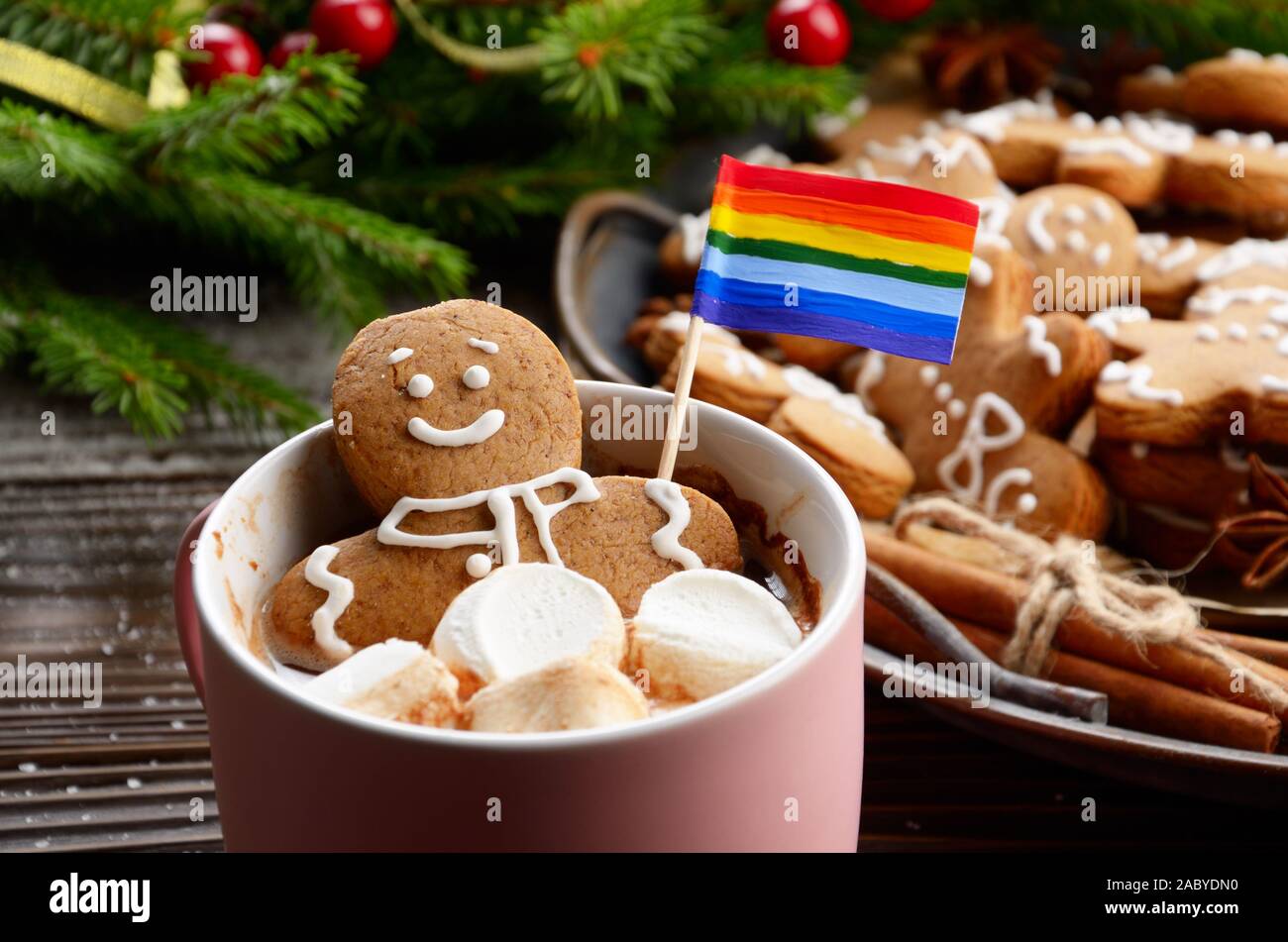 Rosa la tazza con il cioccolato caldo marshmallows e gingerbread man con bandiera arcobaleno sullo sfondo del ramo di abete e il vassoio con i cookie Foto Stock