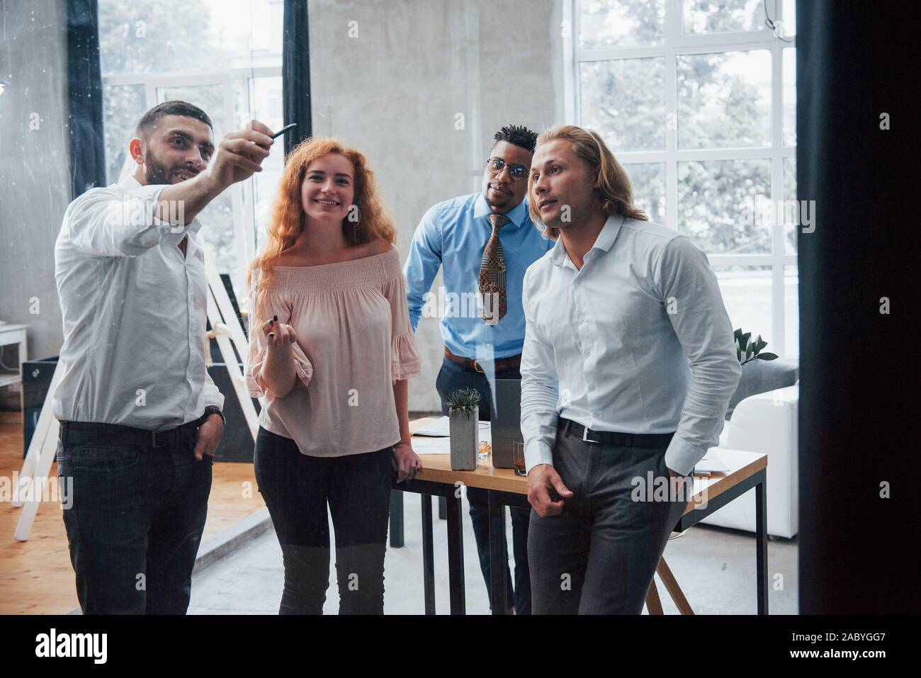 Il team multirazziale discute il loro lavoro iniziando a scrivere sul vetro Foto Stock