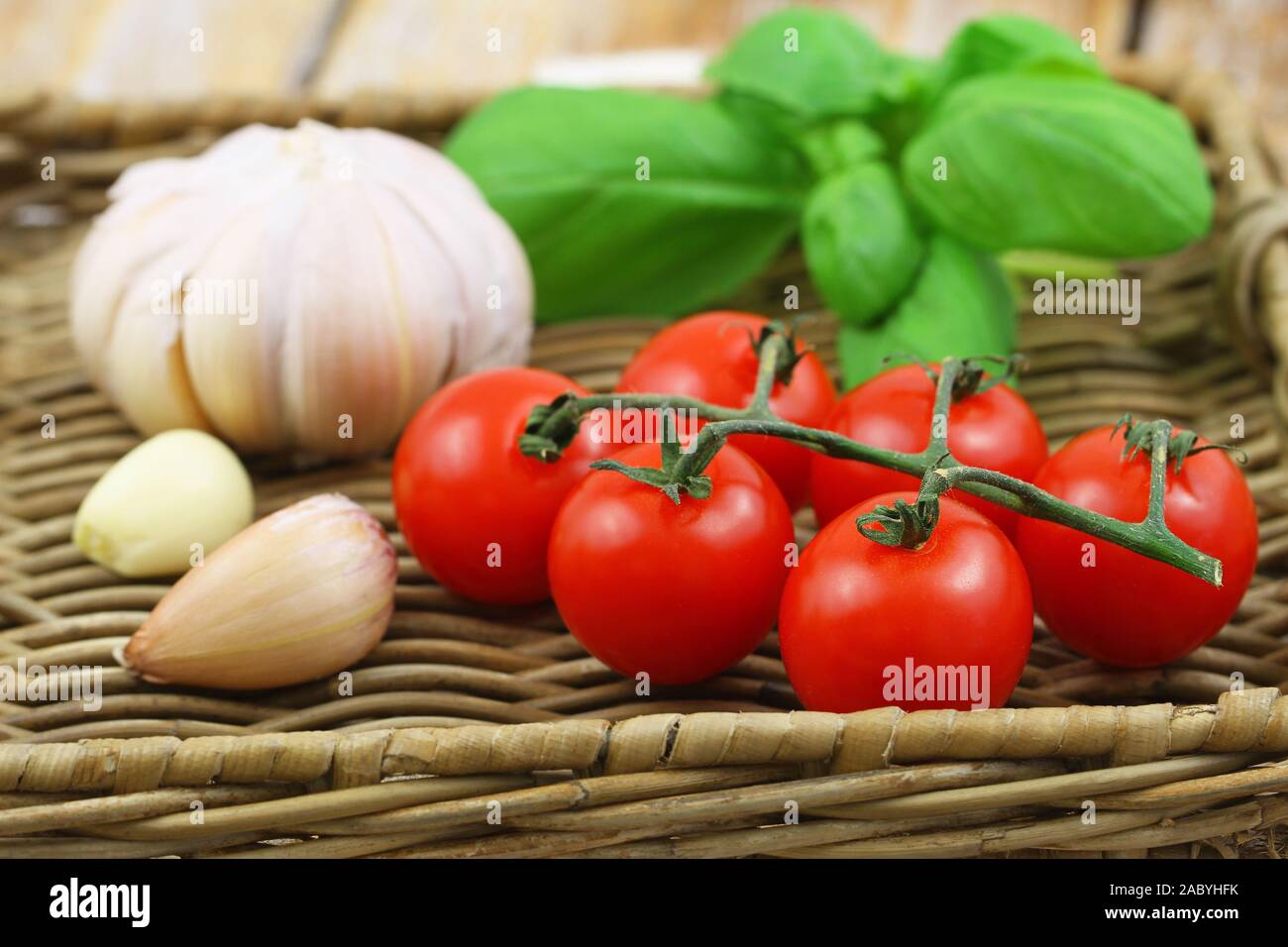Selezione di freschi ingredienti organici per la pasta: pomodori ciliegia, aglio e basilico sul vassoio di vimini Foto Stock