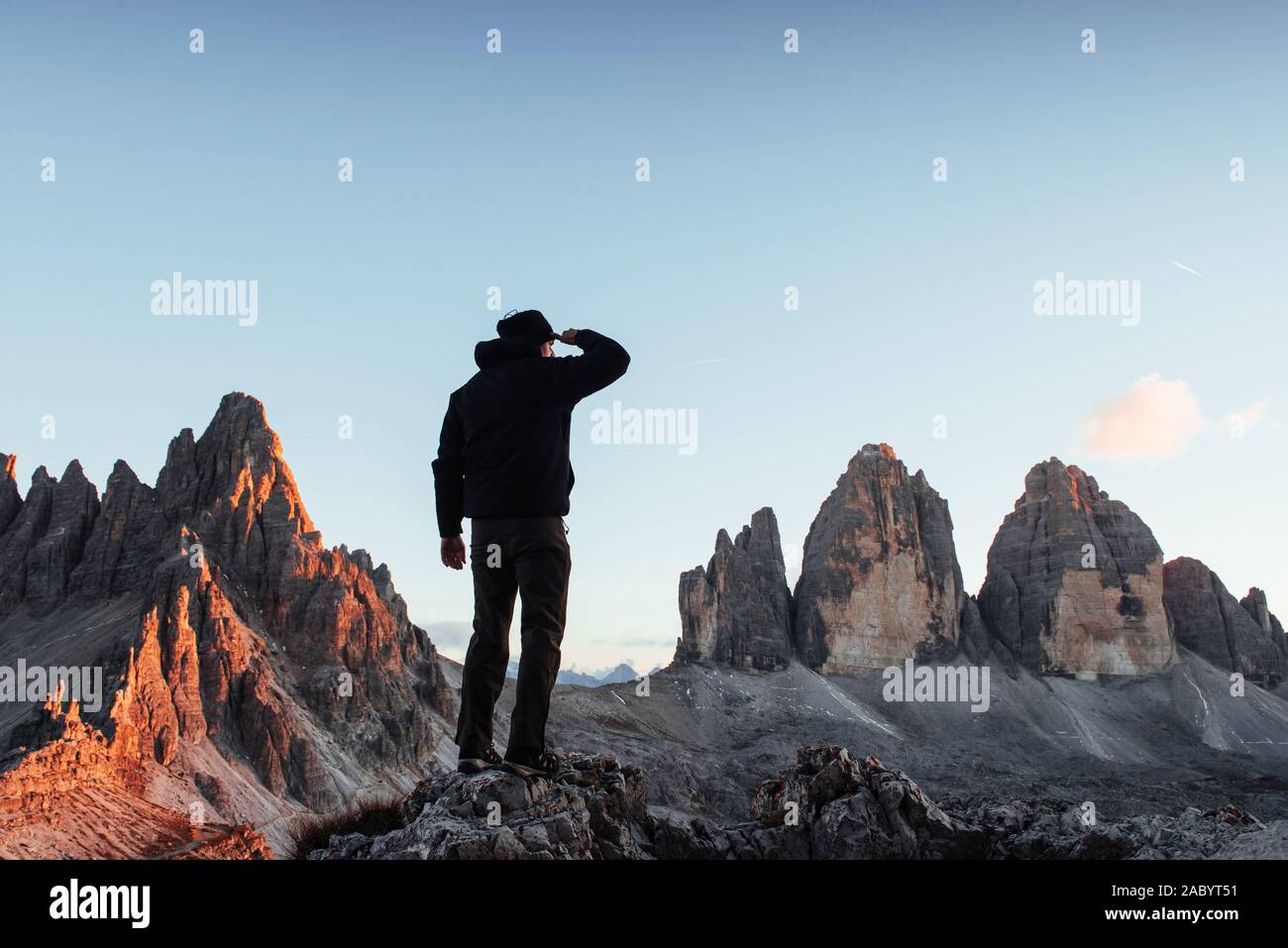 Uomo che guarda lontano con una mano sulla fronte mentre in piedi sulla pietra nella parte anteriore del Paternkofel e tre montagne di suono di avviso Foto Stock