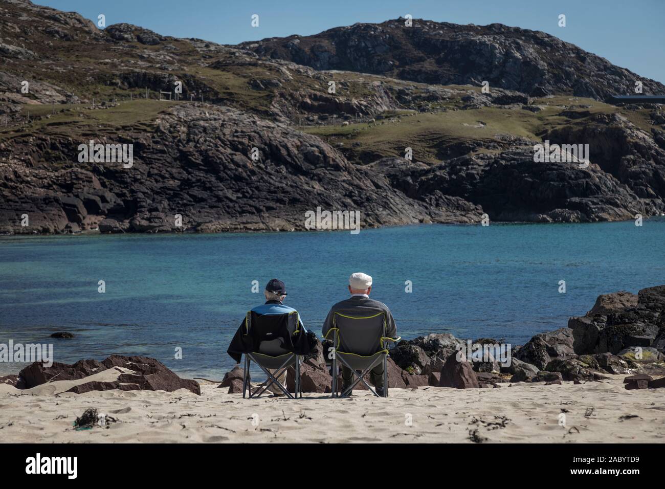 Due anziani rilassarsi in sedie pieghevoli e guardare il mare su una spiaggia di sabbia bianca a Clachtoll, Scozia Foto Stock