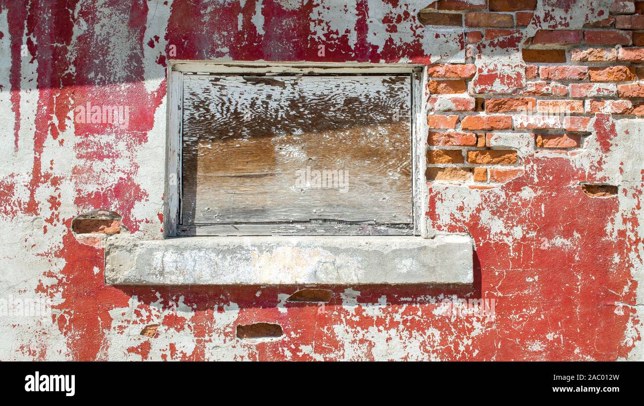 Imbarcati su finestra in una parete di sbriciolamento di un edificio abbandonato con rosso e pareti scrostate mattoni esposta in una giornata di sole Foto Stock