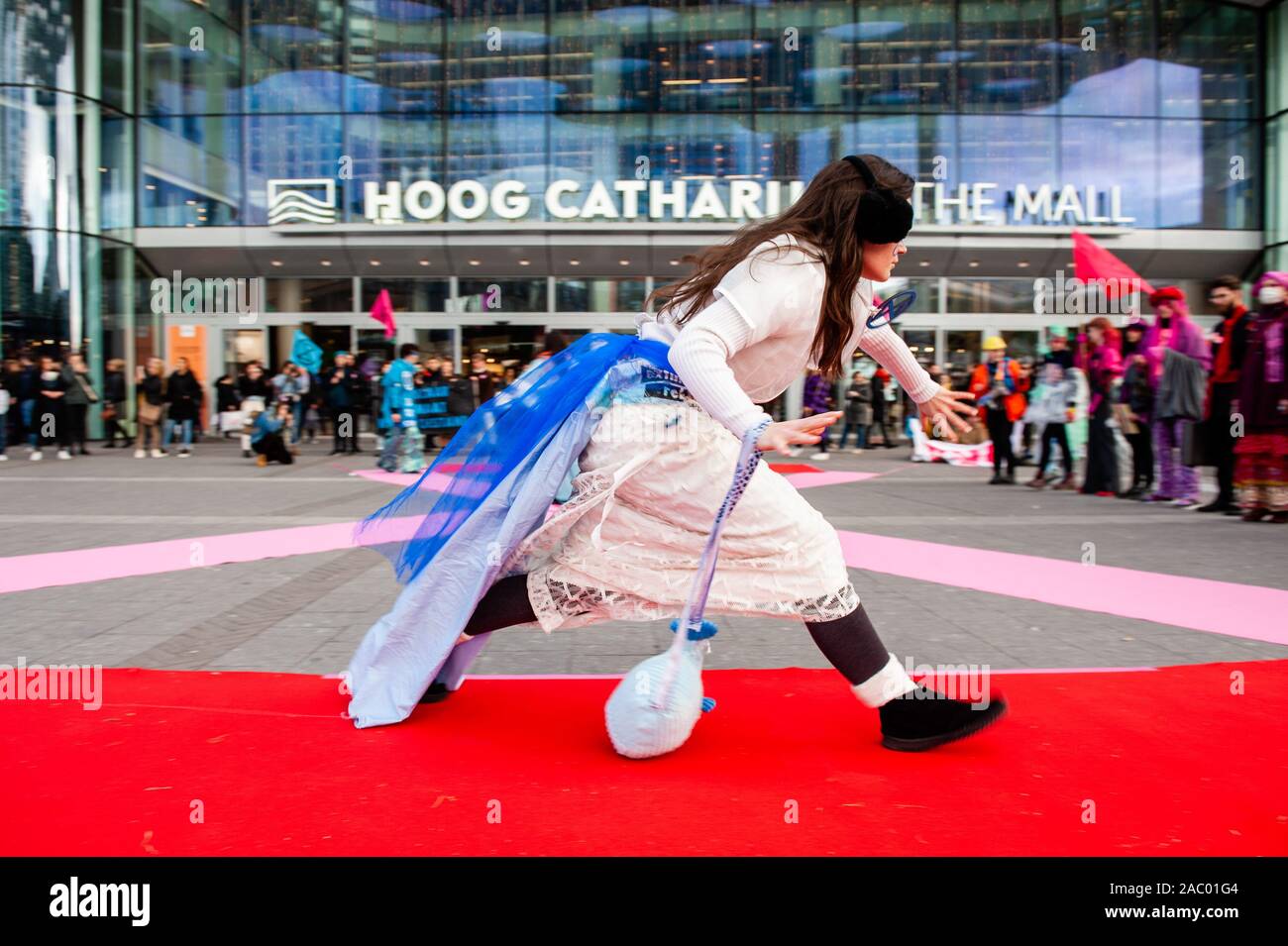 Una femmina modello XR in esecuzione durante la mostra.A Utrecht, estinzione della ribellione Nederland ha organizzato un XR azione di moda, contro il consumismo durante il Black Friday, nella parte anteriore del Hoog Catharijne shopping mall il quale è uno dei la più grande piscina centri commerciali nei Paesi Bassi. Tutti i vestiti che hanno usato era di seconda mano e up-ciclati i vestiti. Questo segue il venerdì per il futuro, la gioventù clima movimenti di sciopero. Foto Stock