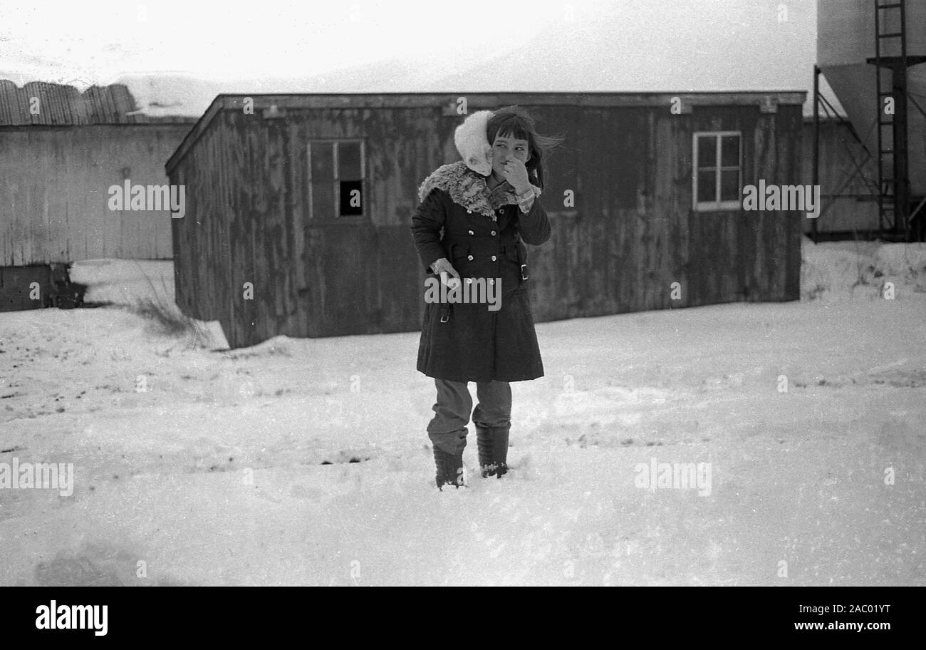 Anni '1980, inverno e un gatto bianco sul cappotto peloso di una giovane ragazza in piedi fuori nella neve in una fattoria nel Midwest America. Foto Stock