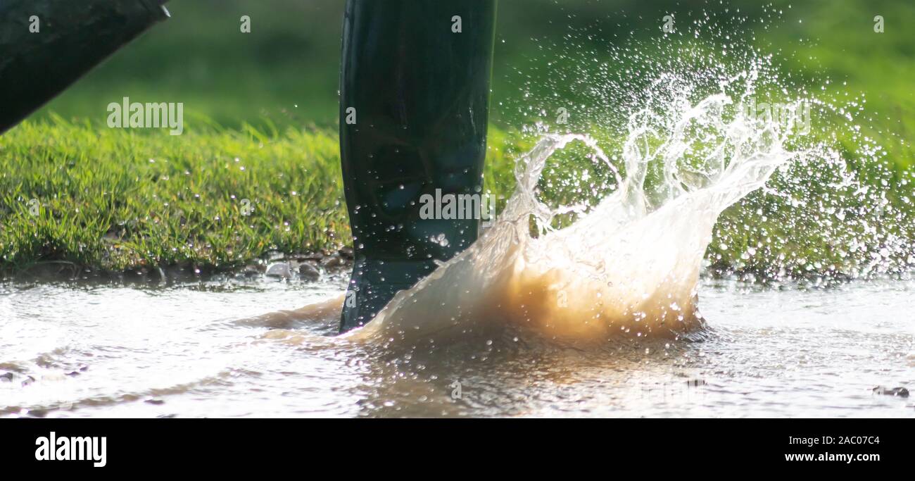 Un uomo o una donna in verde stivali da pioggia a camminare in una grande pozza di fango sotto il sole della luce del mattino copia spazio a lato dell'immagine Foto Stock