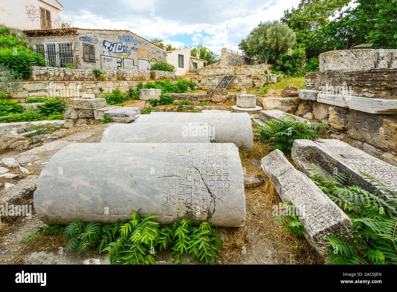 Antiche colonne con iscrizioni lay accanto a un nuovo edificio coperto di graffiti in Atene, Grecia. Foto Stock