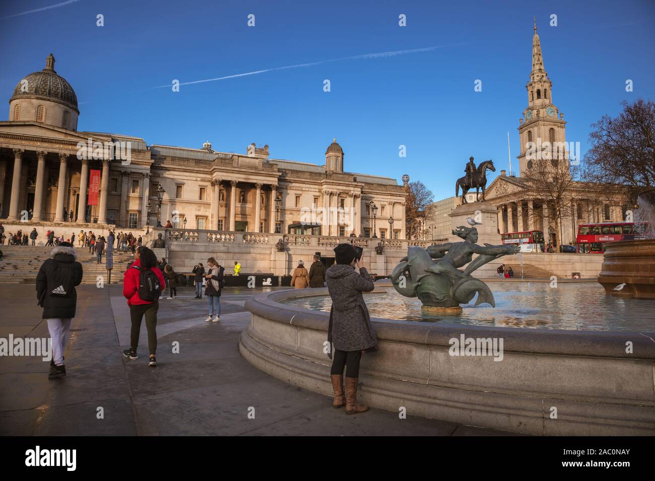 I turisti in Trafalgar Square che mostra la Galleria Nazionale con la statua equestre in bronzo di Re Giorgio IV e St Martin-in-the-Fields Chiesa a b Foto Stock