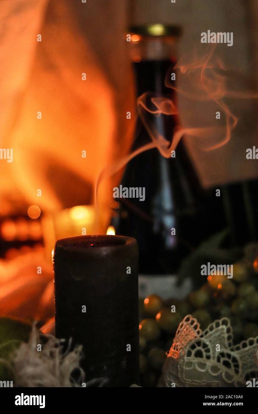 Fumo di candela estinto sul tavolo con bottiglia di vino rosso, uva e luce soffusa su fondo sackcloth. Autunno pieno di soul Foto Stock