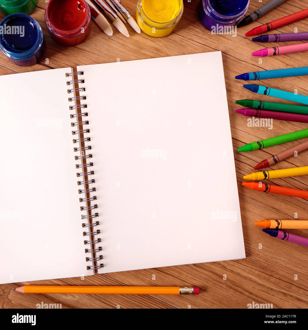 Vuoto bianco notebook aperto su un banco di scuola con varie vernici, matite e pastelli. Foto Stock