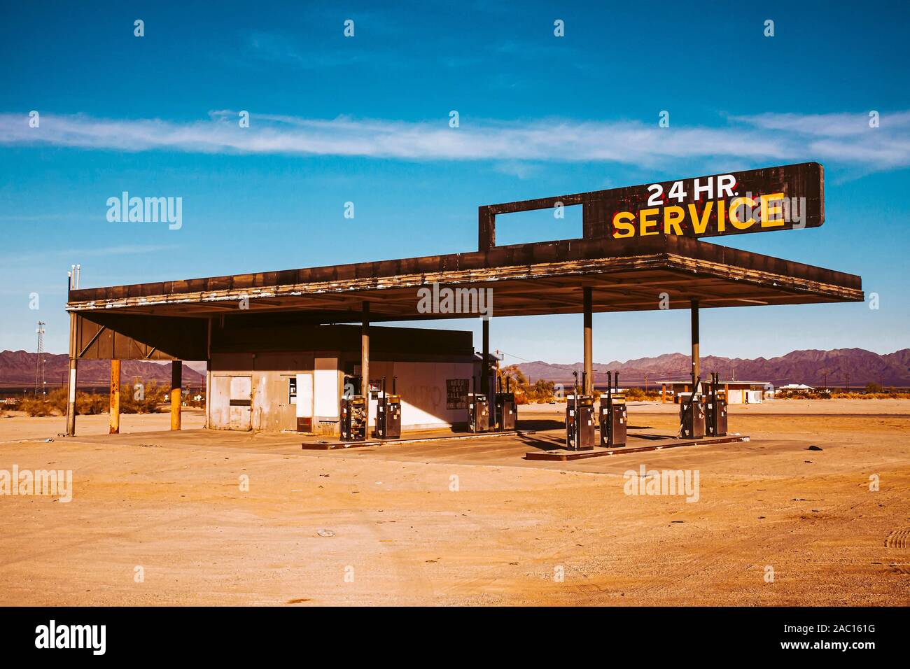 Abbandonata la stazione di gas con la lettura del segno "24 Ore di servizio" con look vintage nel deserto contro il cielo blu e nuvole,, Foto Stock