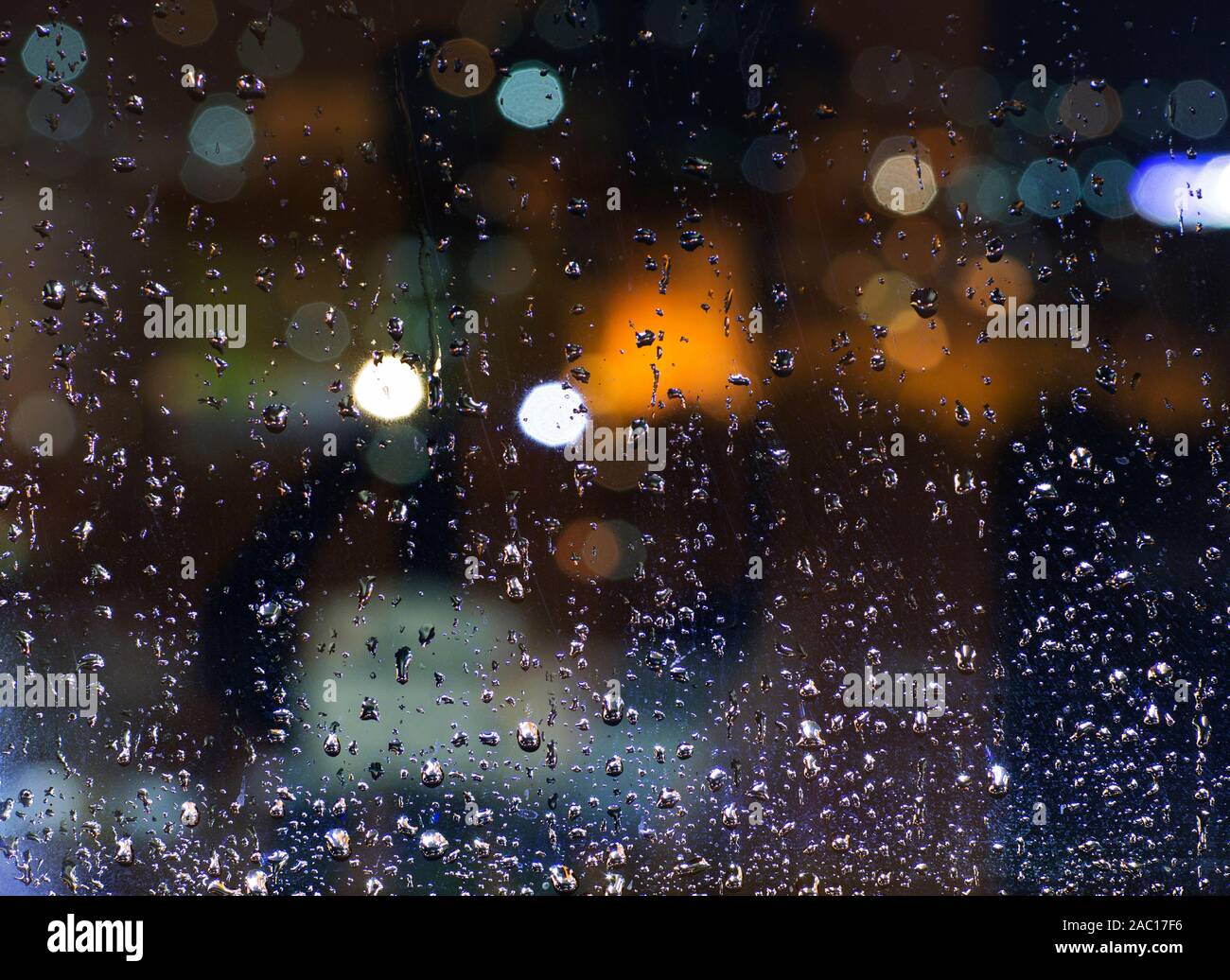La pioggia al di fuori. Gocce di acqua su un vetro di finestra di notte. Il cattivo tempo in città. Luce di Lanterna defocalizzata nel bellissimo bokeh di fondo. Foto Stock