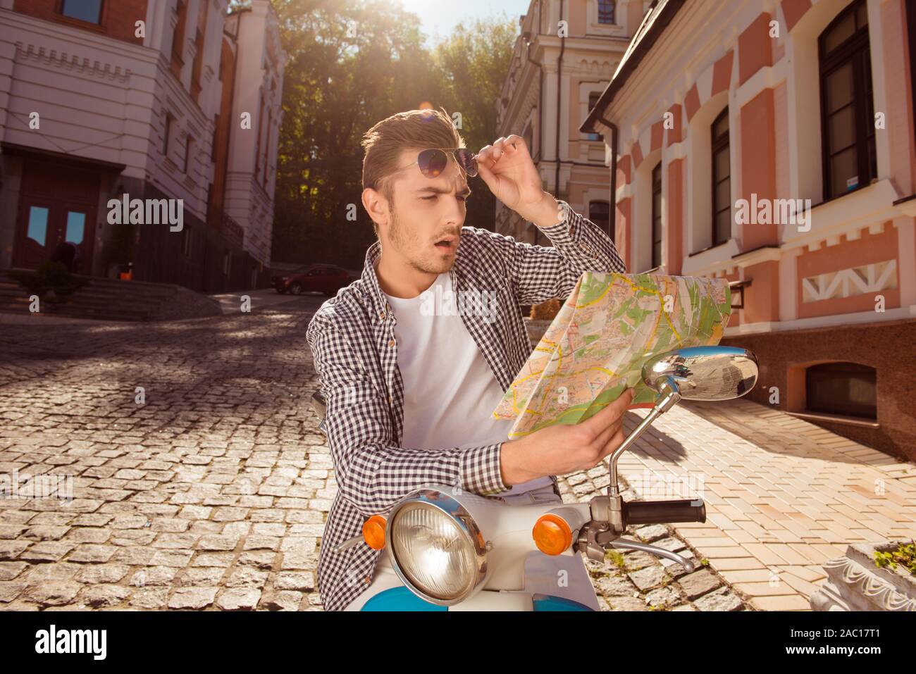 Scioccato bel giovane con gli occhiali seduto sulla moto guardando la mappa Foto Stock