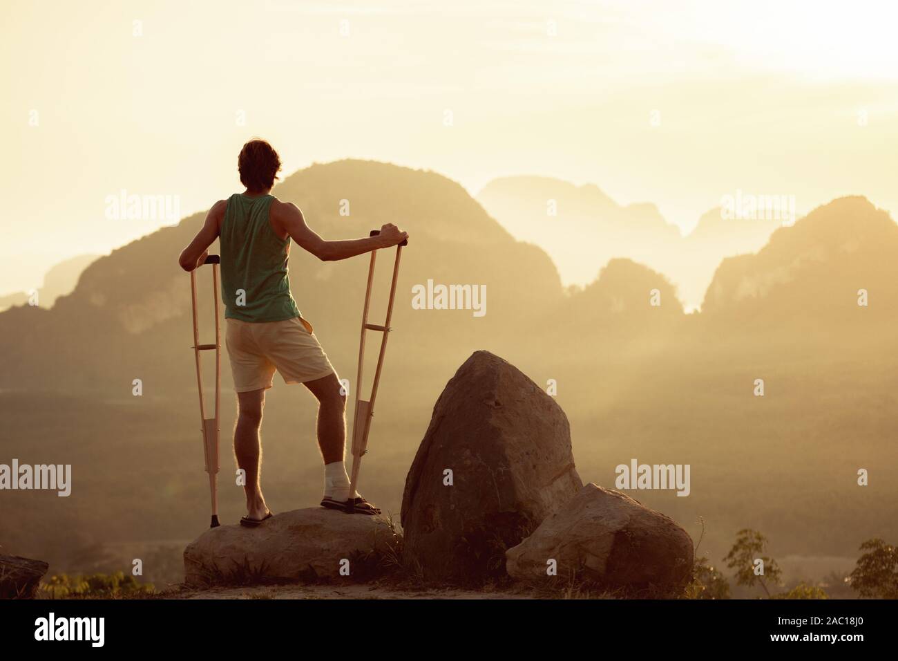 Uomo ferito stand con le stampelle su big rock. Viaggi per disabili popoli concept Foto Stock
